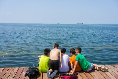 ahşap platform ile kirlenmiş deniz yanında oturan çocuklar s işareti kaldırın.
