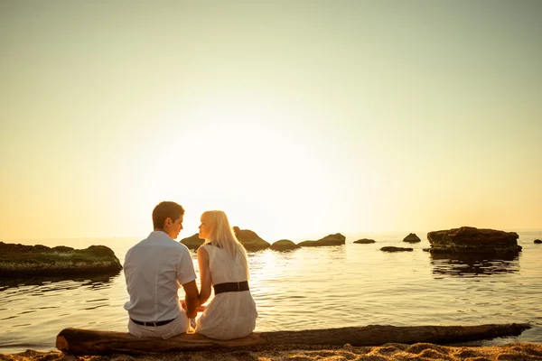 Par sitter och tittar på varandra på stranden vid soluppgång — Stockfoto