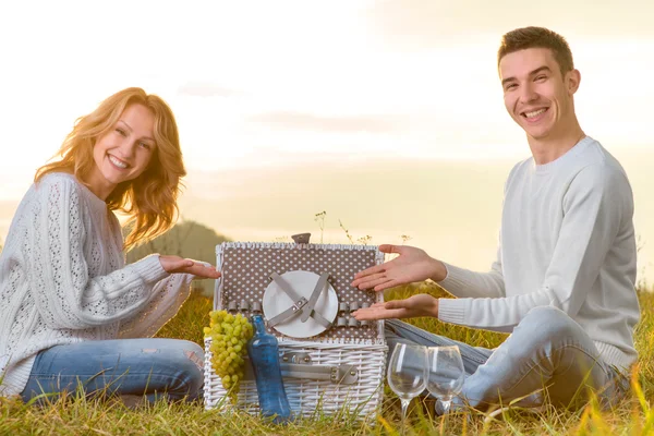 Couple assis et présentant panier blanc pique-nique sur une herbe — Photo