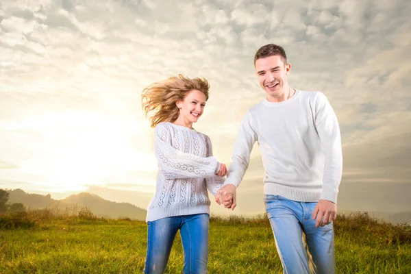 Coppia che corre, ride e si tiene per mano sotto il cielo — Foto Stock