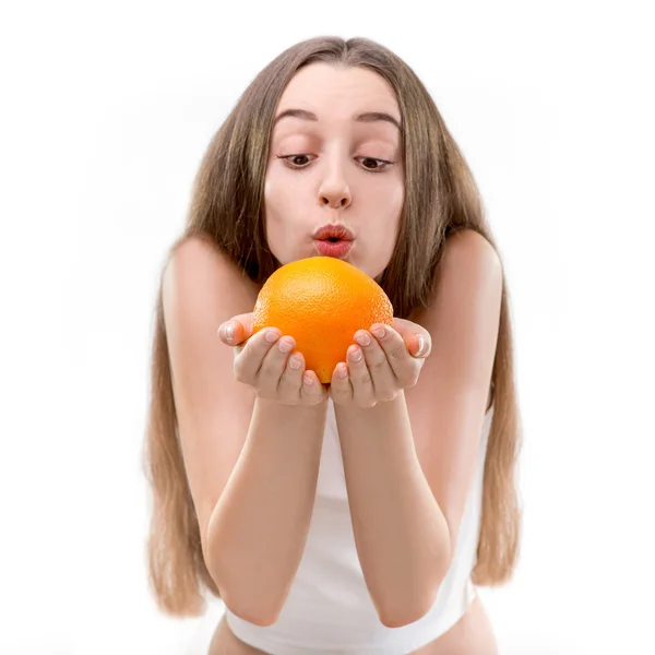 Девушка держит оранжевый и дует на оранжевый на белом фоне — стоковое фото