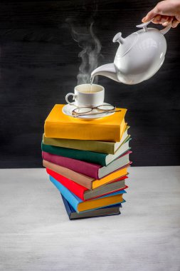 Stack of colorful books with a cup of tea on it and teapot pouri clipart