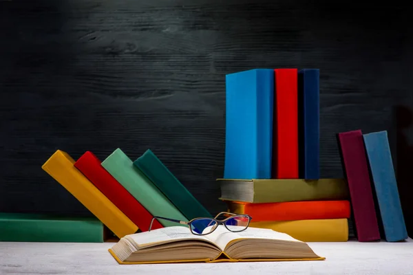 Opened book on the table with glasses and another colorful books — Stock Photo, Image