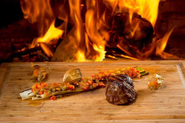 Heerlijke rundvlees steaks op houten bureau en brand op achtergrond — Stockfoto