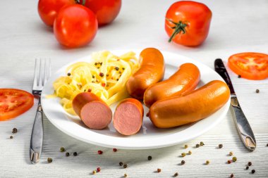 Sausages with pasta and tomatoes on a plate on white desk clipart