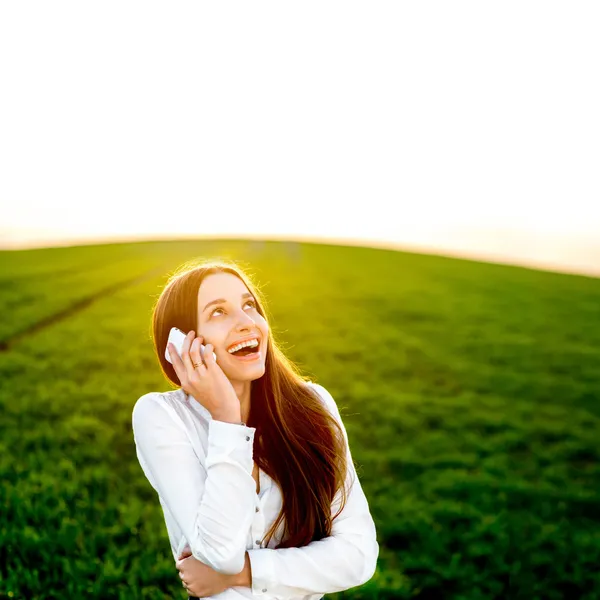 Young woman laughing in talking in smart phone in the green fiel — Stock Photo, Image