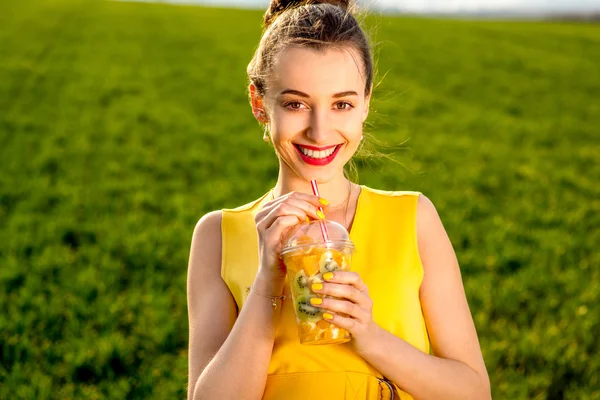 Jovem mulher sorrindo com frutas em copo transparente em gras verdes — Fotografia de Stock