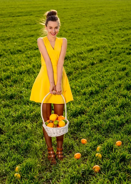 Mujer joven con cesta llena de frutas sonriendo en greenfield de —  Fotos de Stock