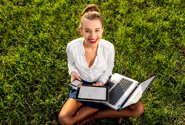 Femme d'affaires souriante avec ordinateur portable, tablette et téléphone assis sur — Photo