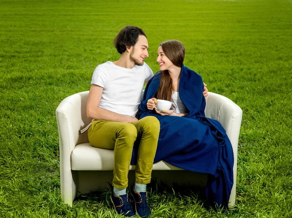 Jeune couple amoureux assis sur le canapé sur le champ vert — Photo