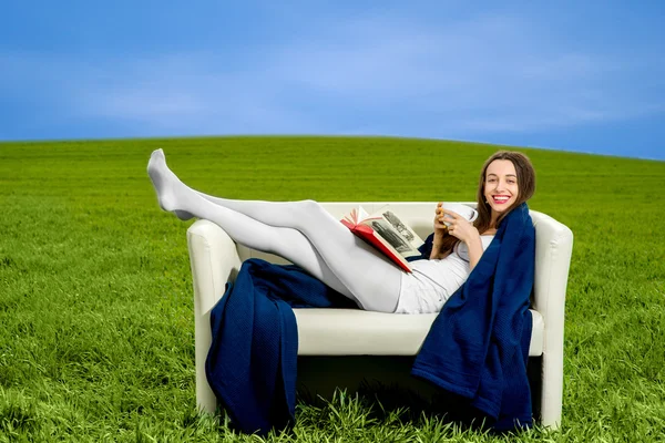 Chica leyendo libro y beber café en el sofá en el verde —  Fotos de Stock