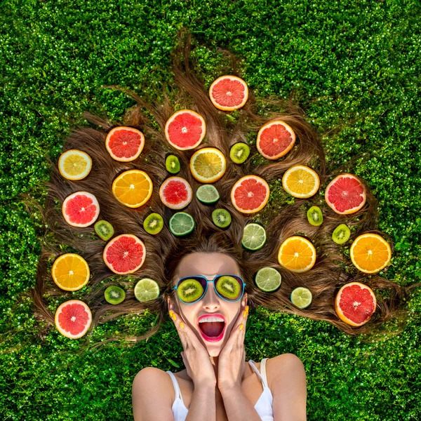 Schöne Frau auf dem Gras liegend mit Früchten um ihr Haar ein — Stockfoto