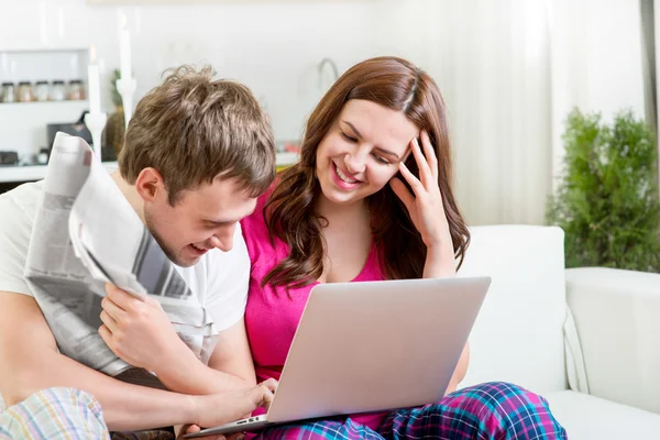 Pareja joven casada en pijama sentada en el sofá leyendo noticias — Foto de Stock