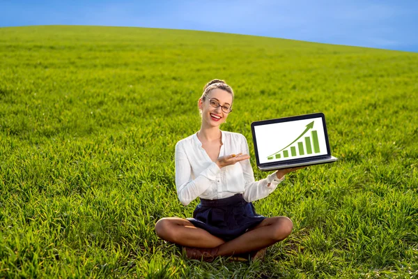 Giovane donna che mostra diagramma di crescita sul computer portatile sul fi verde — Foto Stock