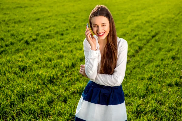 Fiatal mosolygó nő beszél a zöld mezőben szúró telefon — Stock Fotó