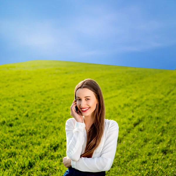 Jovem sorrindo mulher falando no telefone inteligente no campo verde — Fotografia de Stock