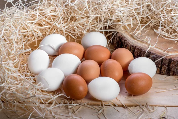 Bruine en witte eieren in het stro nest op houten achtergrond — Stockfoto