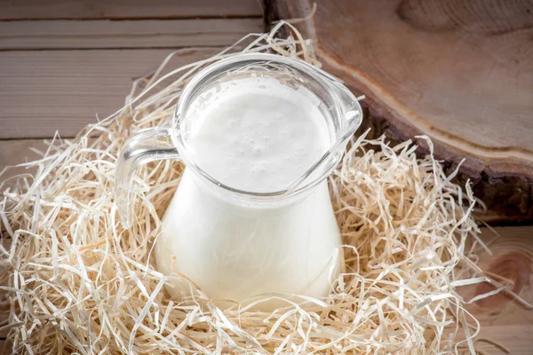 Lait dans la cruche transparente sur bureau en bois avec foin, vue vers le haut — Photo