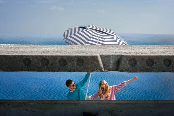 Casal se divertindo com grande guarda-chuva no fundo da água azul — Fotografia de Stock