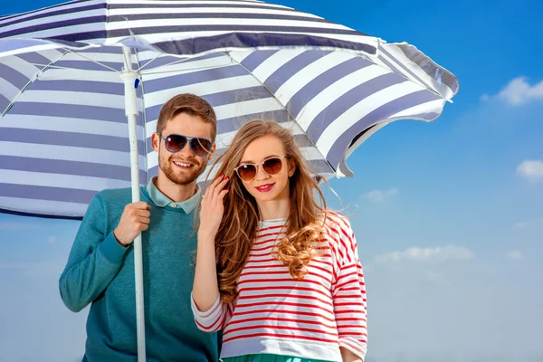 Jeune couple souriant sous le parapluie sur fond bleu ciel — Photo