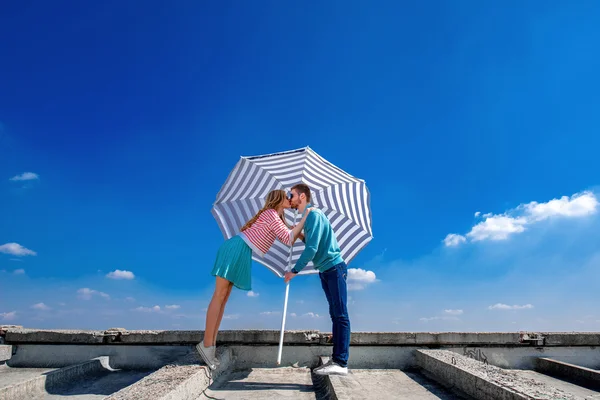 Młoda i ładna para całuje na dachu pod parasol o — Zdjęcie stockowe