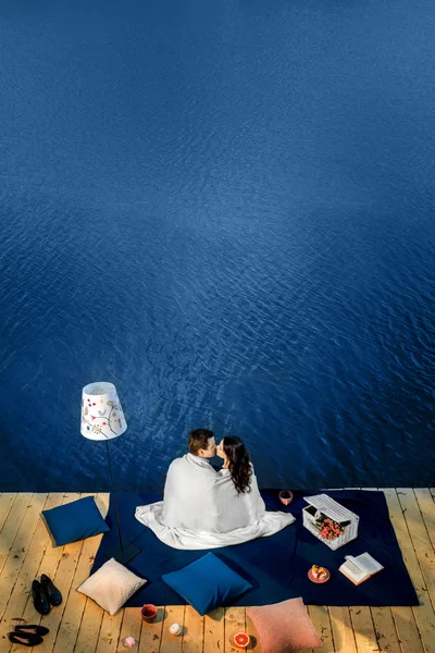 Couple covered by blanket sitting on terrace near the water — Stock Image Couple covered by blanket sitting on terrace near the water Royalty Free Stock Photos