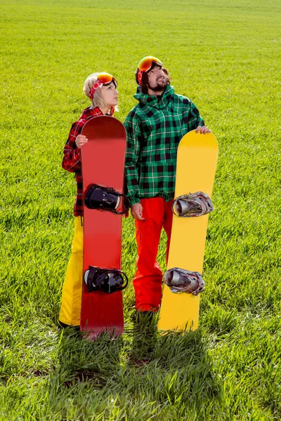 Couple in sport wear with snowboards standing on the grass and w — Stock Photo, Image