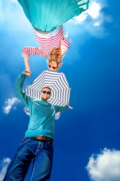 Молодая пара держится за руки и смотрит вниз с пляжным зонтиком — стоковое фото