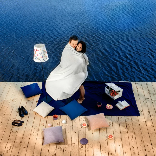 Casal coberto por cobertor em pé no terraço perto da água — Fotografia de Stock