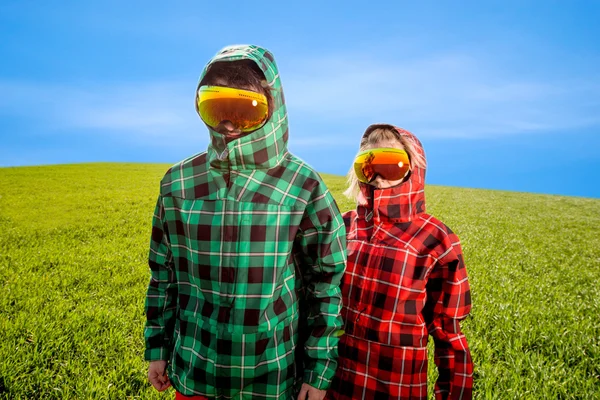 Couple in the ski suits standing in the green field — Stock Photo, Image