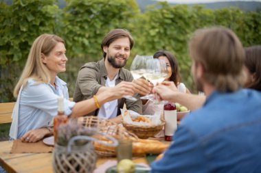 Dostlar üzüm bağlarının yanındaki piknikte şarap içiyorlar.