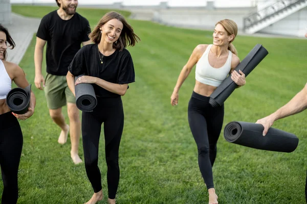 Lidé chodí s fitness rohožemi na zelené louce — Stock fotografie