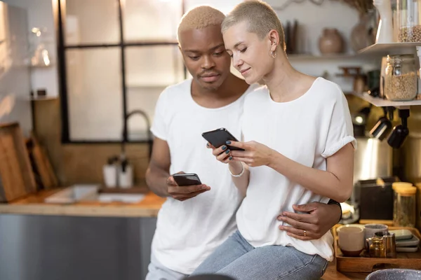 Pareja usando el teléfono móvil en la cocina casera —  Fotos de Stock