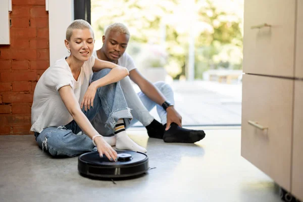 Par som sitter på golvet med robotdammsugare — Stockfoto