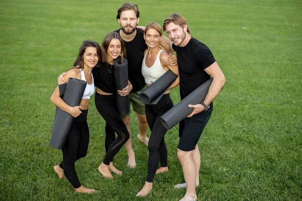 Mensen met fitnessmatten staan in groene weide — Stockfoto