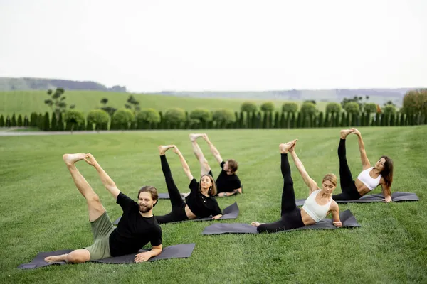 Gente practicando yoga en colchonetas de fitness en el prado — Foto de Stock