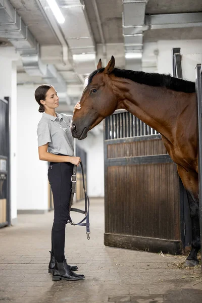 Female horseman feeding her horse in stable