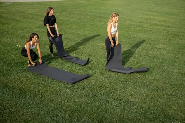 Vriendinnen zetten fitnessmatten op groene weide — Stockfoto