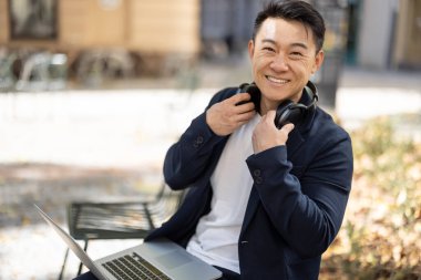 Asyalı iş adamı dışarıda dizüstü bilgisayarda çalışıyor.