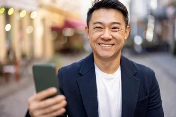 Homem asiático segurando smartphone e olhando para a câmera — Fotografia de Stock