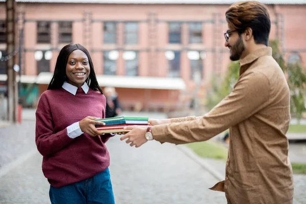 Indiase man geven boeken naar zwart meisje buiten — Stockfoto