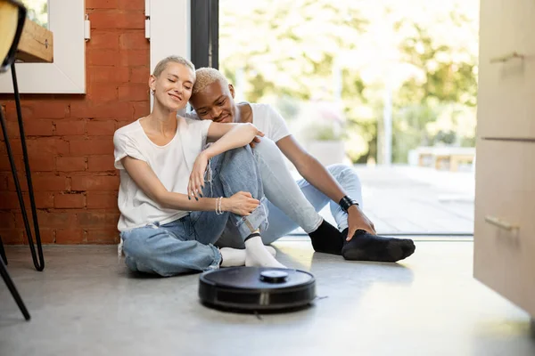 Пара сидить на підлозі з роботом-пилососом — стокове фото