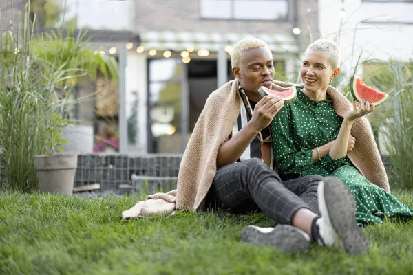 Multiracial couple eat watermelon in their garden — Stock Photo, Image