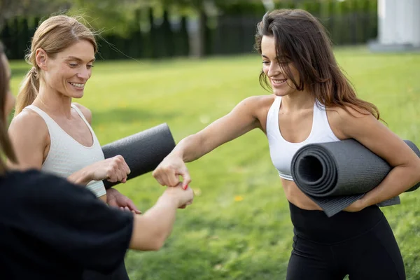 Meisjes met fitness matten stoten vuisten op weide — Stockfoto