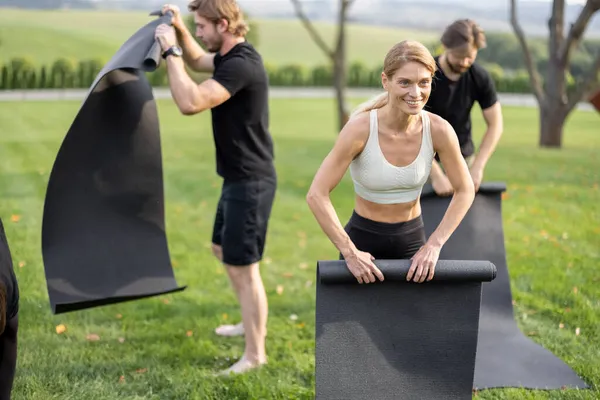 La gente dobla las alfombras de fitness después del entrenamiento en el prado — Foto de Stock