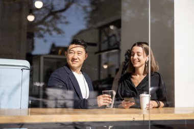 Çok ırklı bir çift kafedeki masada kahve içiyor.