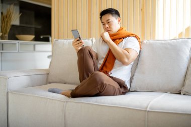 Hasta Asyalı adam öksürüyor ve akıllı telefon kullanıyor.