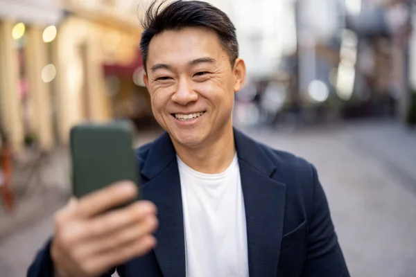 Homem asiático segurando smartphone e olhando para a câmera — Fotografia de Stock
