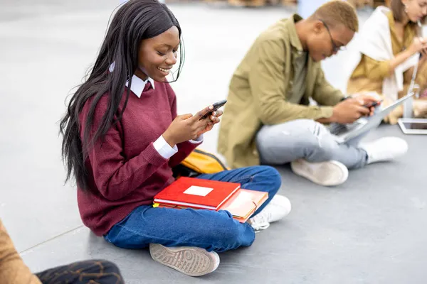 Studenti sedí a používají smartphony na asfaltu — Stock fotografie