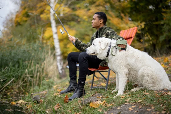 Muž rybaření v blízkosti psa na břehu řeky nebo jezera — Stock fotografie
